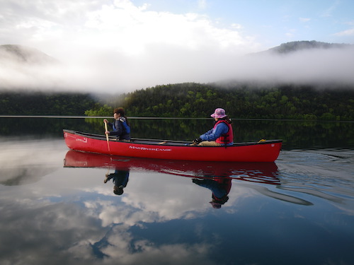 早朝の然別湖を赤いカヌーに乗って漕いでいる様子を写したツアー写真
